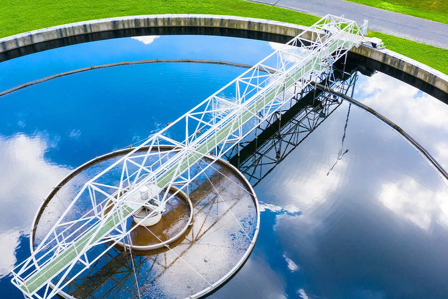 Aerial view of a wastewater treatment tank with metal bridge, reflecting blue sky and clouds
